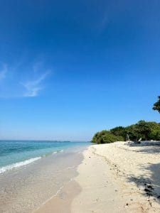 Beautiful Lombok beach with white sand and clear blue water under a bright sky.