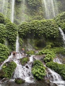 Lush green waterfall with visitors enjoying the scenic view in Lombok.