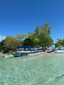 Boat anchored on clear waters at Gili Nanggu with trees and blue sky.
